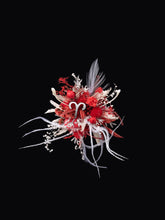 The Aries Flower Ring by CAMELLIA showcases a vibrant, abstract floral arrangement with red, white, and pink elements handcrafted from feathers and curly ribbons on a black background. This customizable piece adds a unique touch to any setting.